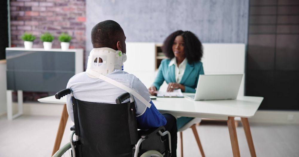 A man in a wheelchair is sitting at a desk talking to a woman.