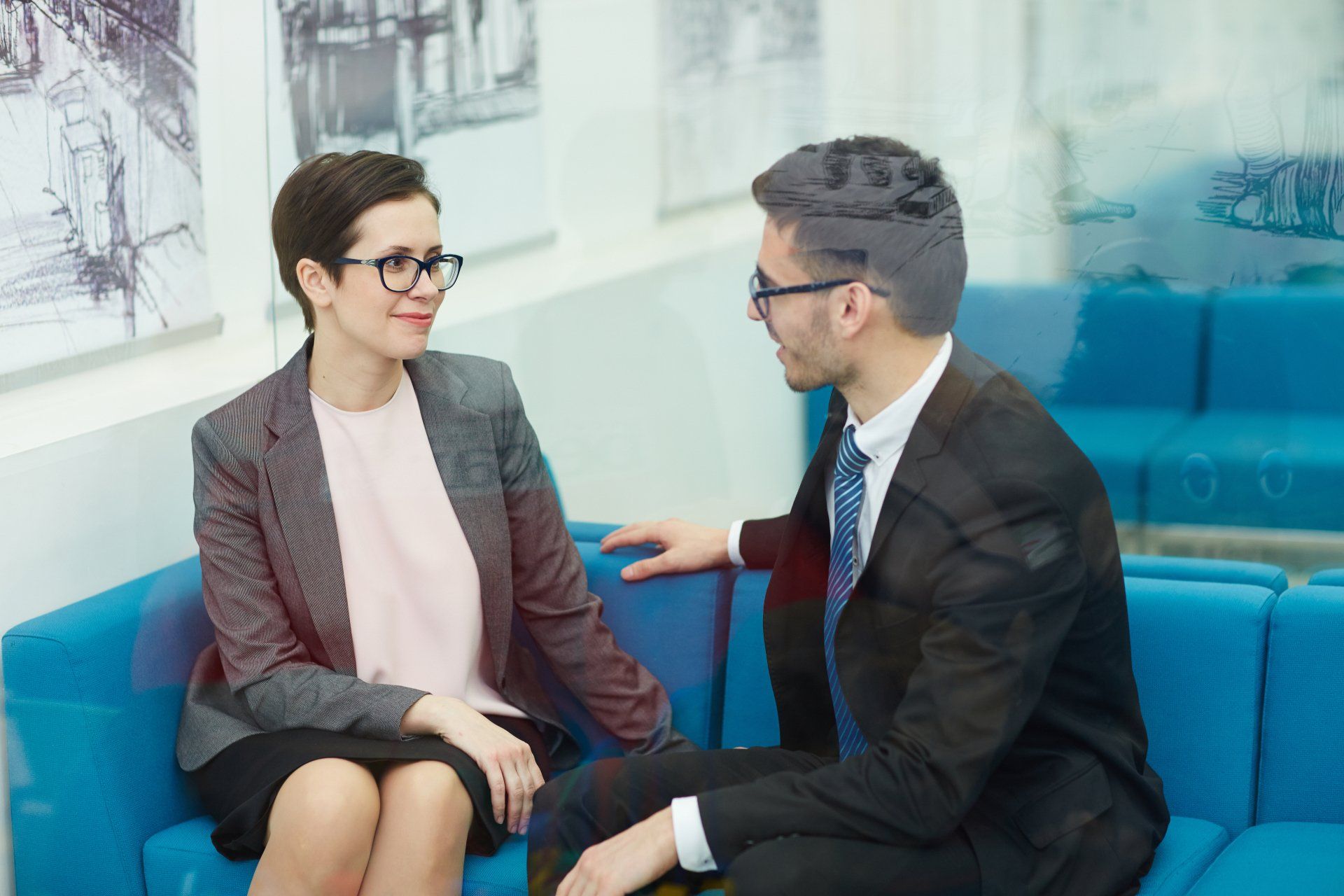 A man and a woman are sitting on a blue couch talking to each other.