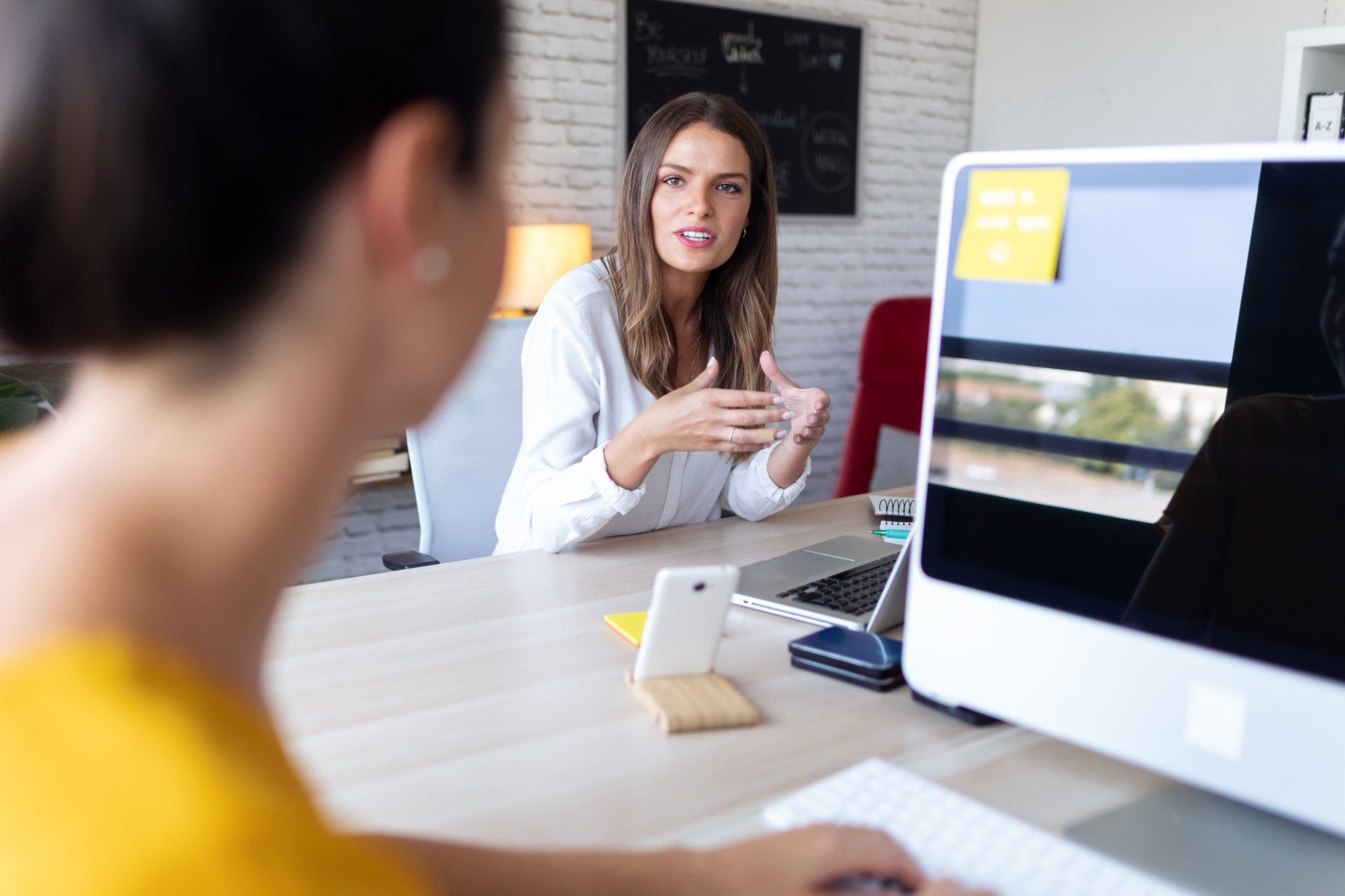 A woman is sitting at a desk talking to another woman.