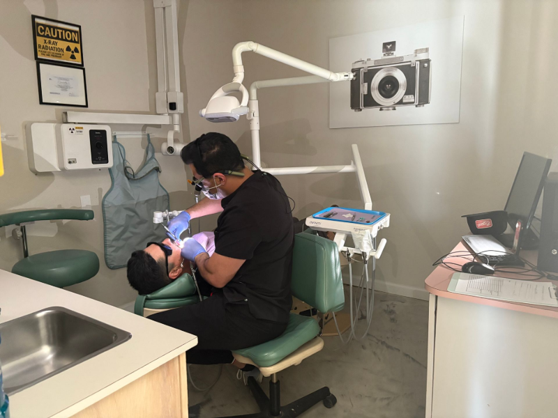 Dentist examining a patient's mouth in a dental office. The patient is reclined in a chair.