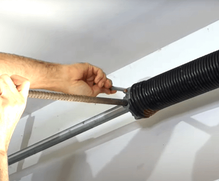 A person is adjusting and fixing a garage door spring with a screwdriver.