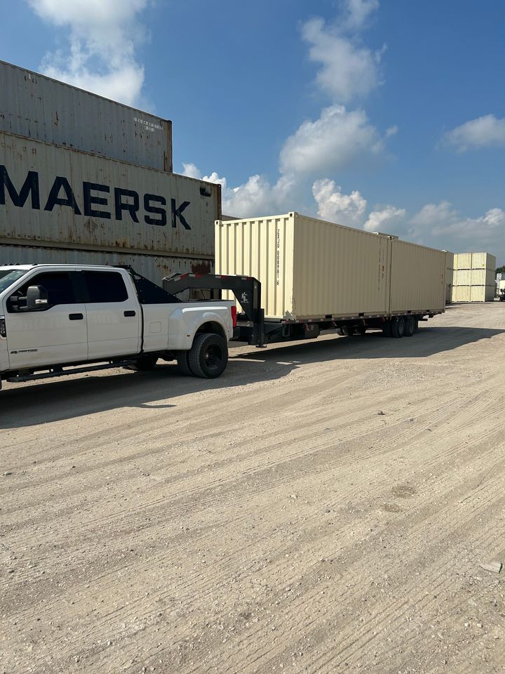 Truck carrying shipping containers, parked in a lot, cloudy sky overhead.