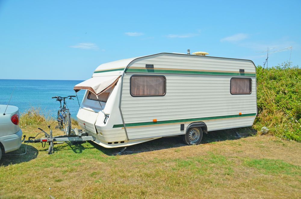 White Camper Trailer Parked Near Ocean With Bicycle Attached. Sunny Day — Total Caravan Repairs in Nabiac, NSW