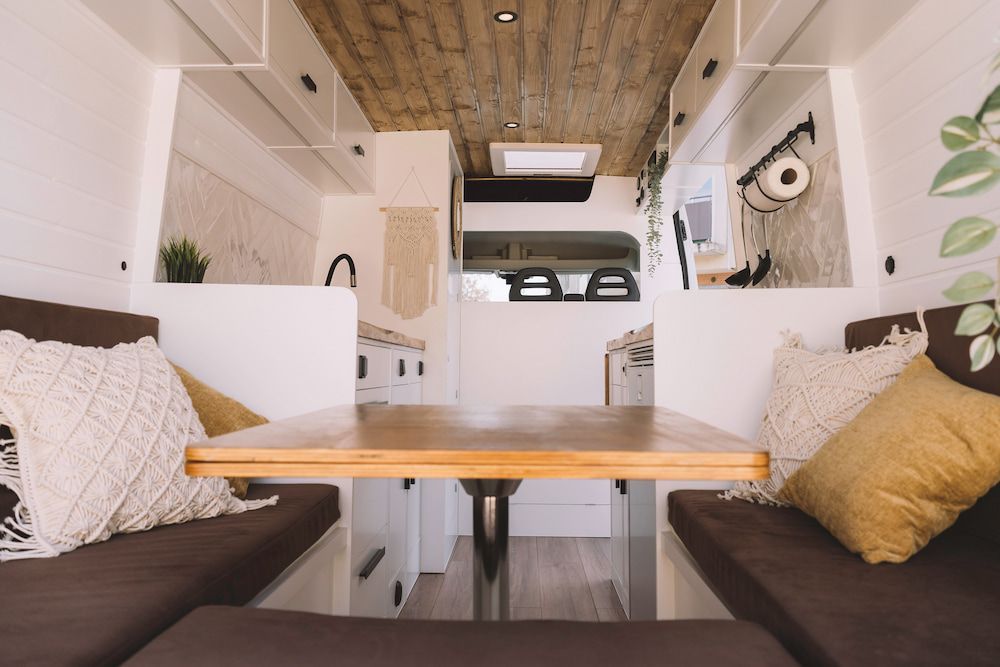Cozy Van Interior With a Wooden Table, Brown Cushions, and Decorative Pillows — Total Caravan Repairs in Forster, NSW