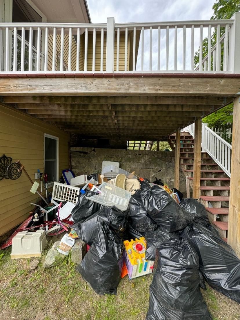 A pile of trash bags is sitting under a deck next to a house.