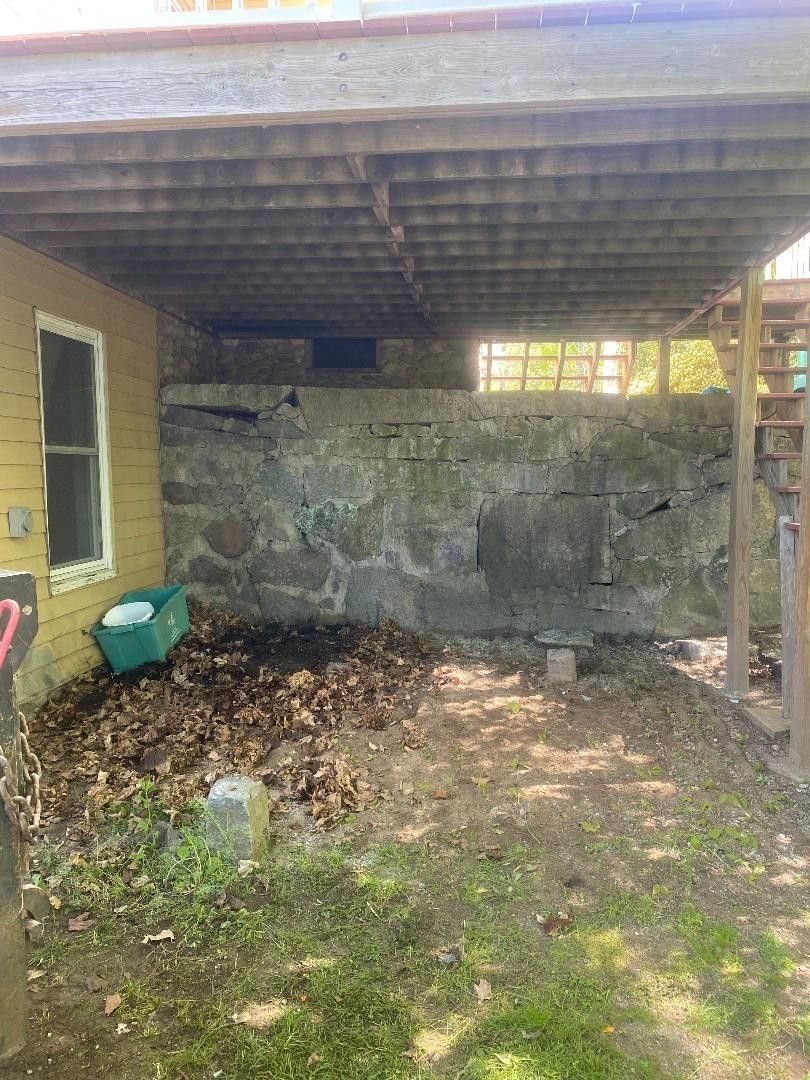 The backyard of a house with a stone wall and a wooden deck.