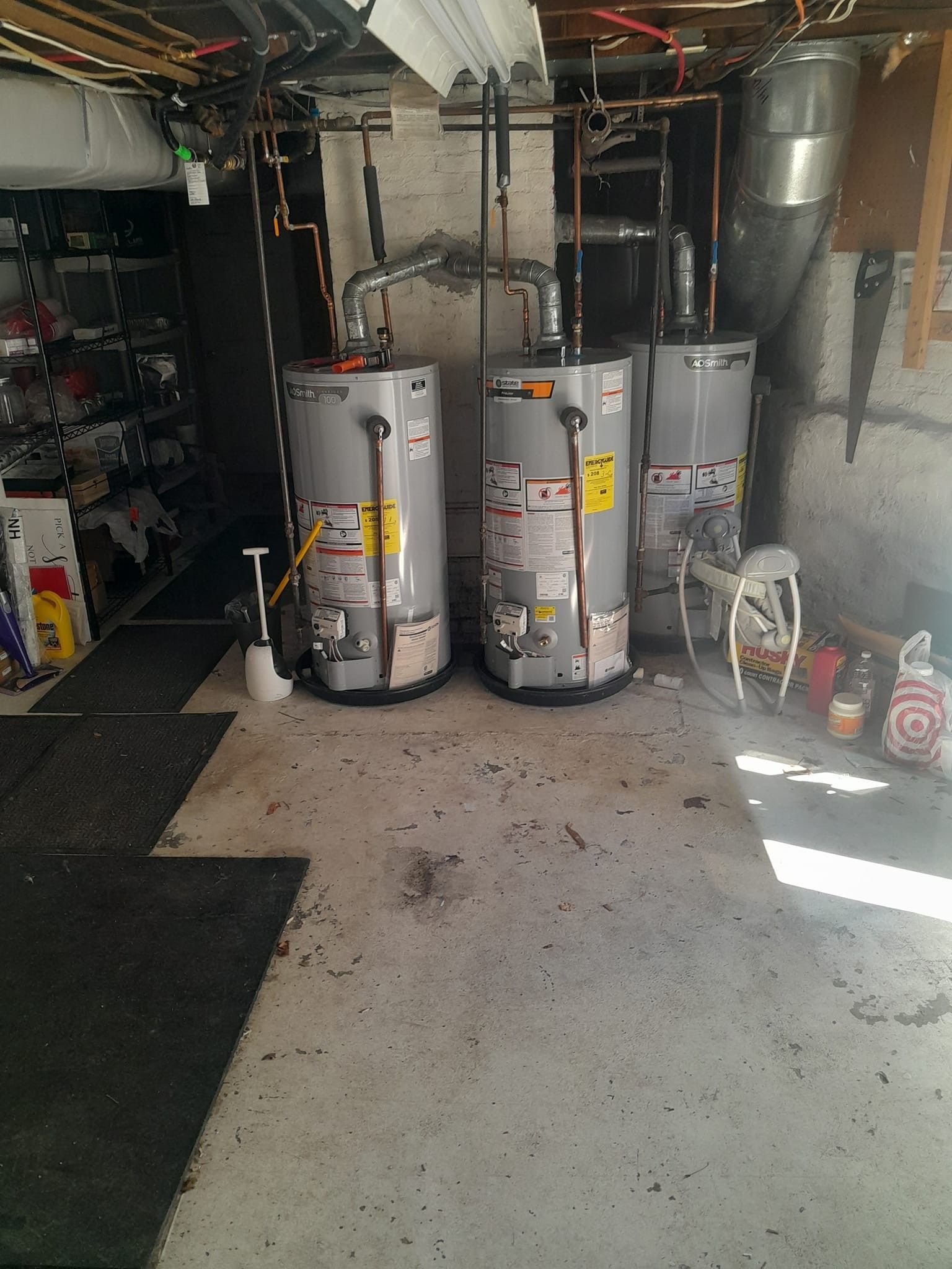 Two water heaters are sitting in a basement next to each other.