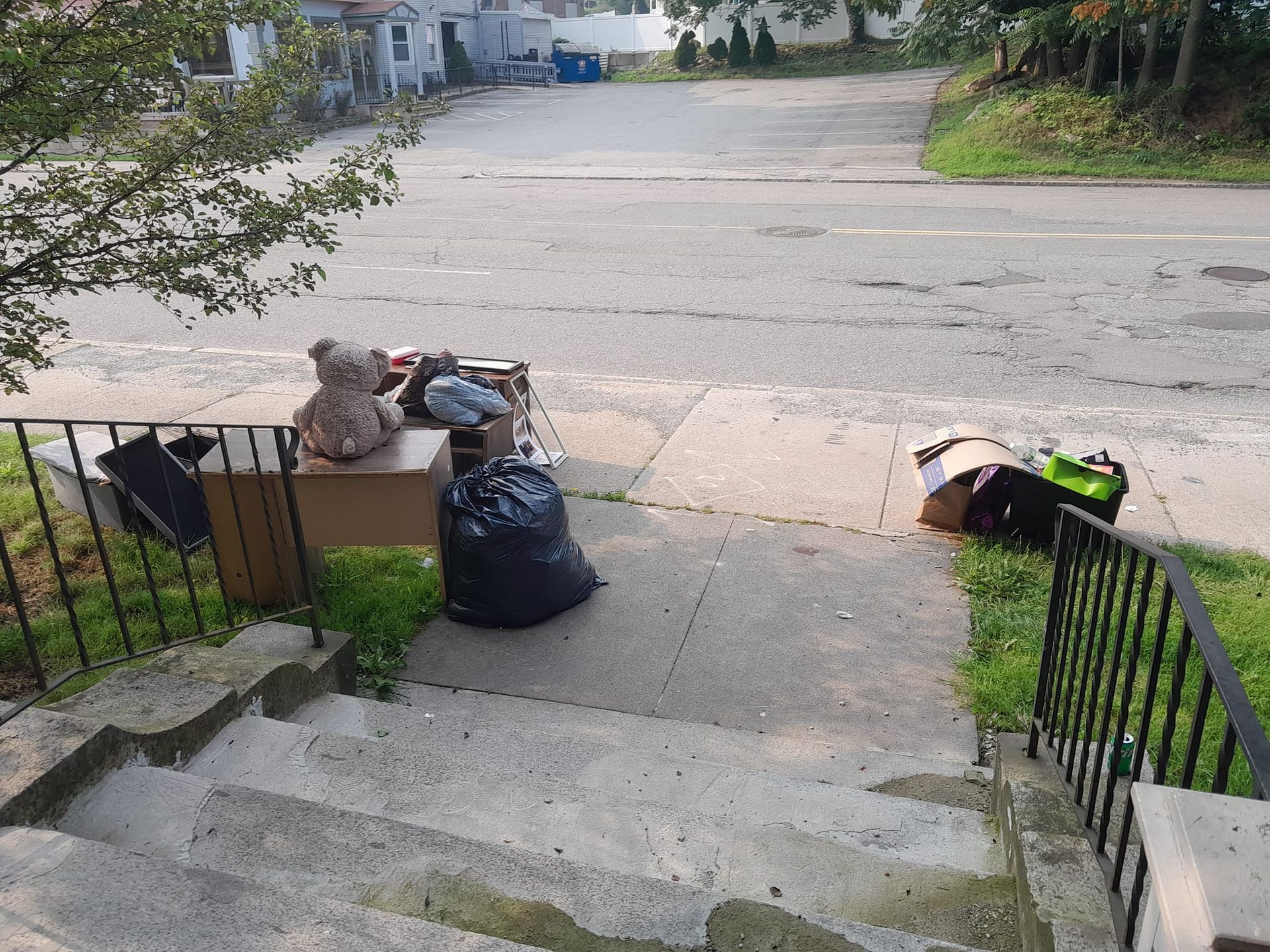 A pile of trash is on the sidewalk next to a set of stairs.