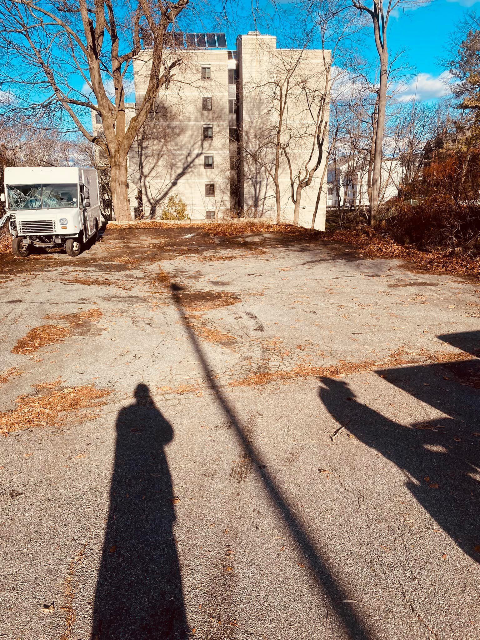 A shadow of a person is cast on the ground in a parking lot.