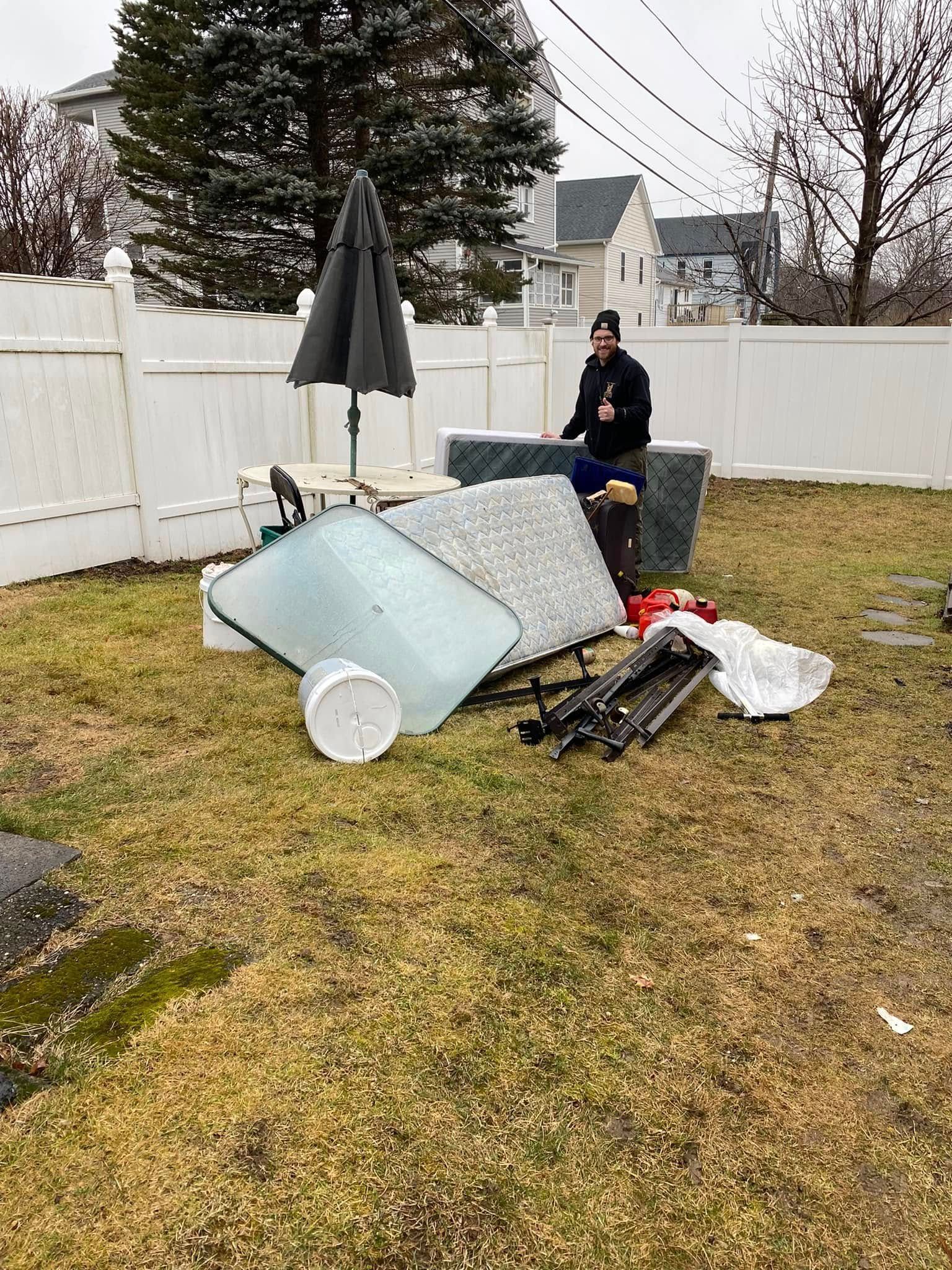 A man is standing in front of a pile of junk in a backyard.