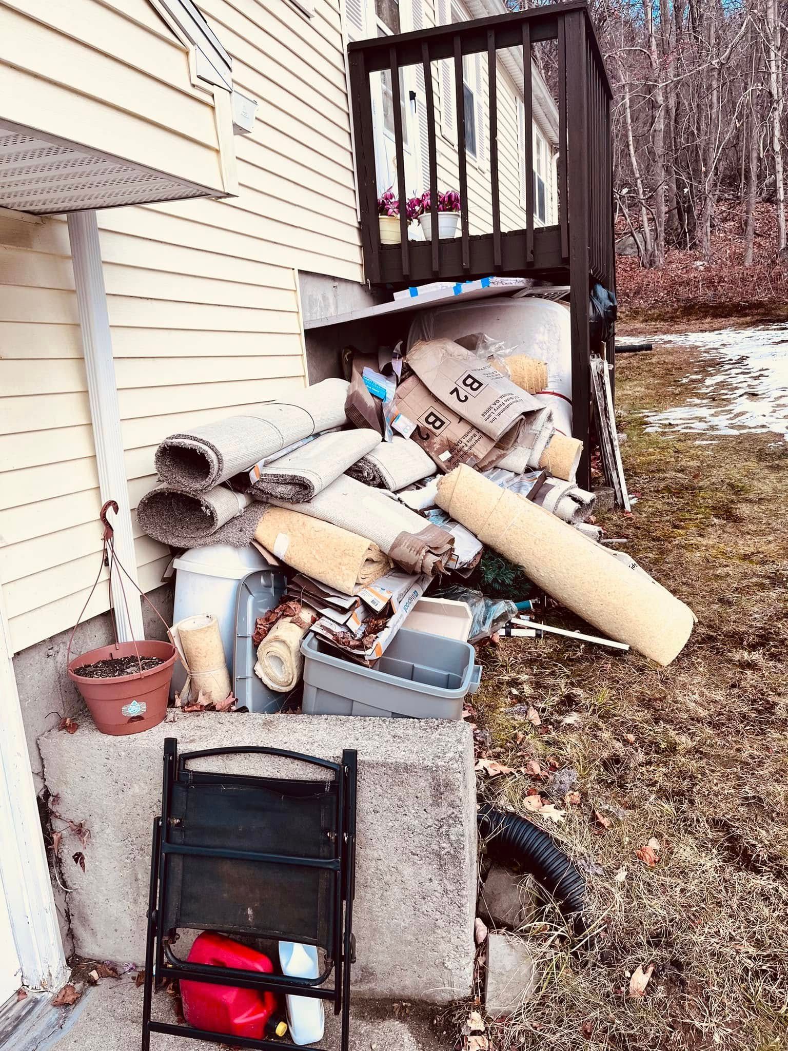 A pile of trash is sitting on the side of a house next to a chair.