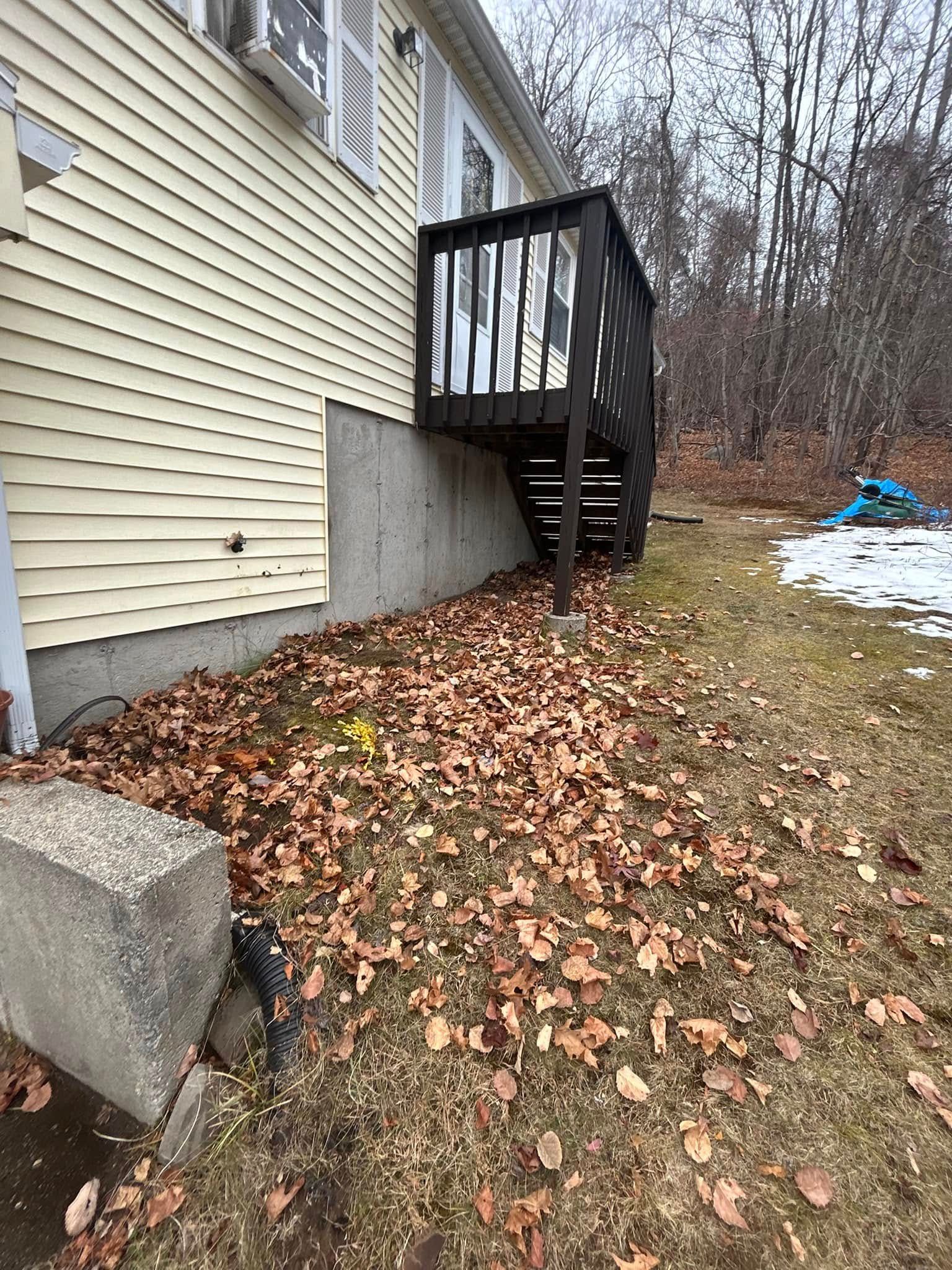 A house with a deck on the side of it and a lot of leaves on the ground.