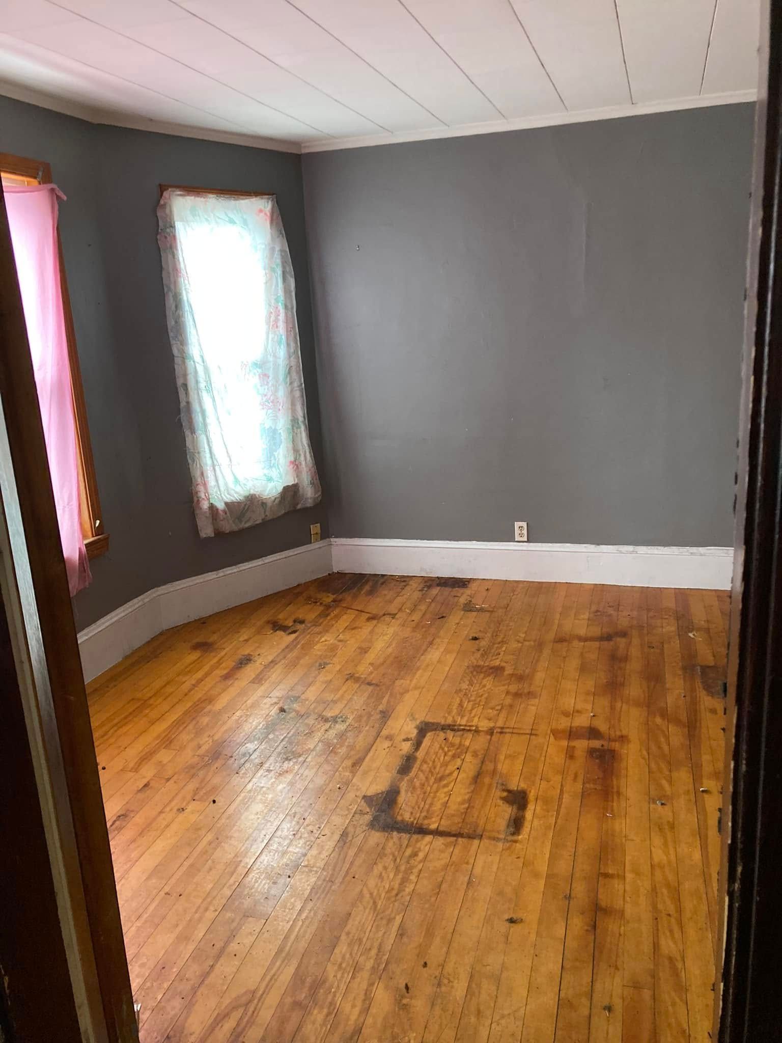 An empty room with a wooden floor and gray walls.
