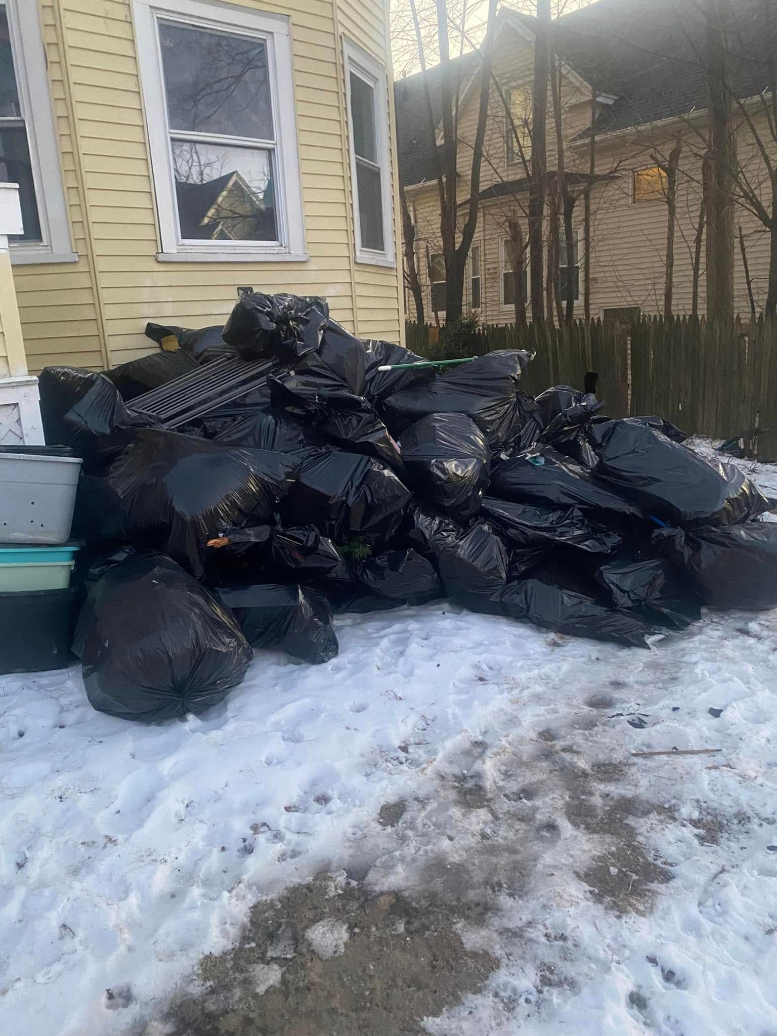 A pile of trash bags is sitting in the snow in front of a house.
