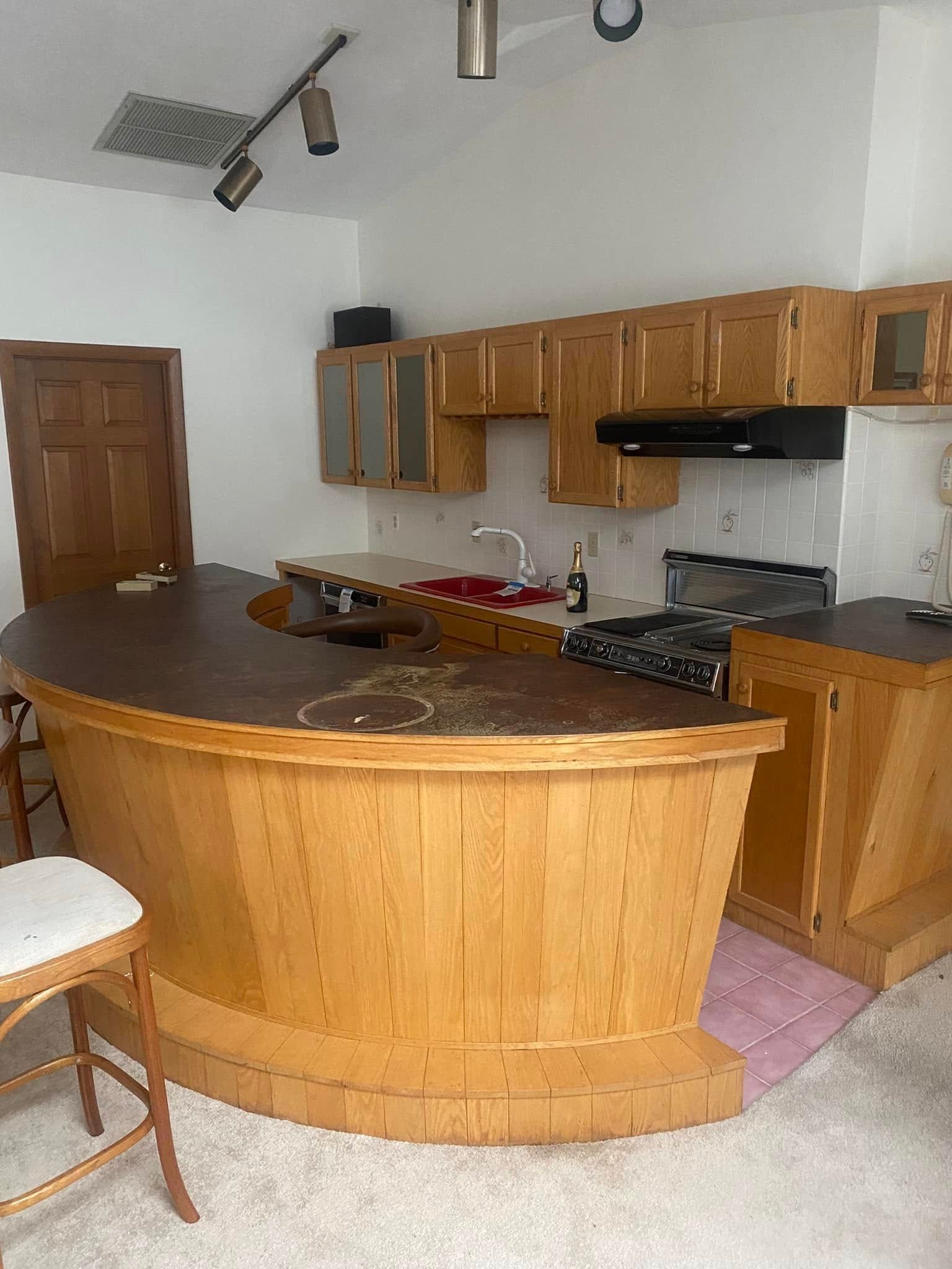 A kitchen with wooden cabinets , a stove , a sink and a bar.