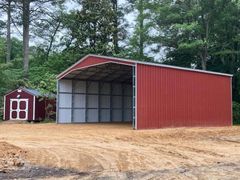 Red metal shed with open front; small shed to the left; dirt and trees in background.