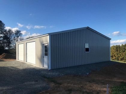 Gray metal building with two garage doors and a side door, gravel ground, and blue sky.