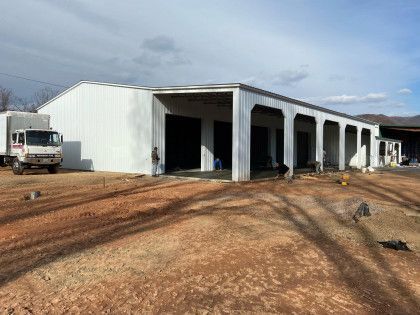 White warehouse with open bays, truck parked outside, people working.
