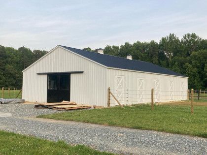 White barn with a black roof and sliding door, gravel driveway, and a wooden fence.