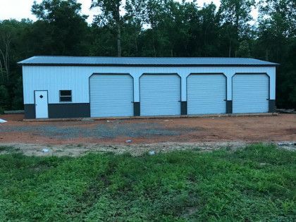 A white metal garage building with four bays, a side door, and a small window, set against a tree line.