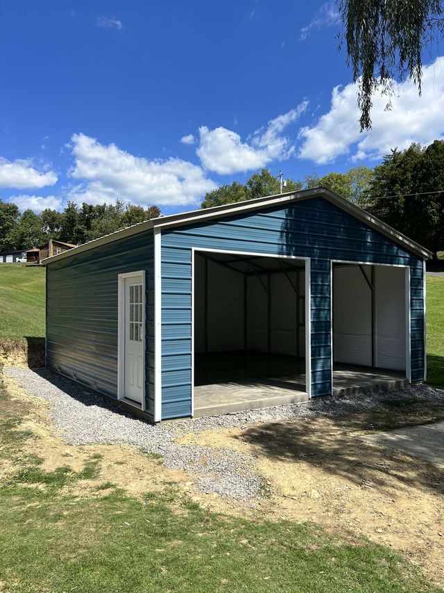 Tan metal two-car garage with white doors, side entry, set on asphalt, surrounded by greenery.