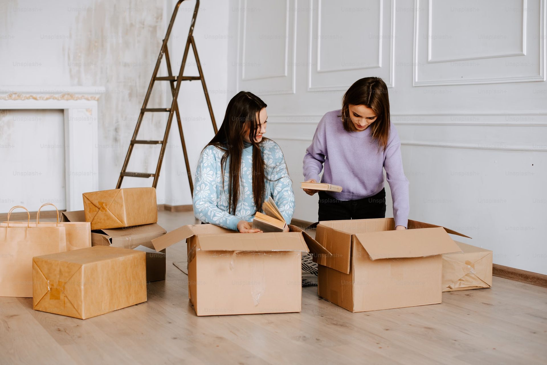 Two women carefully packing fragile items into cardboard boxes, preparing for storage at Durango Storage.