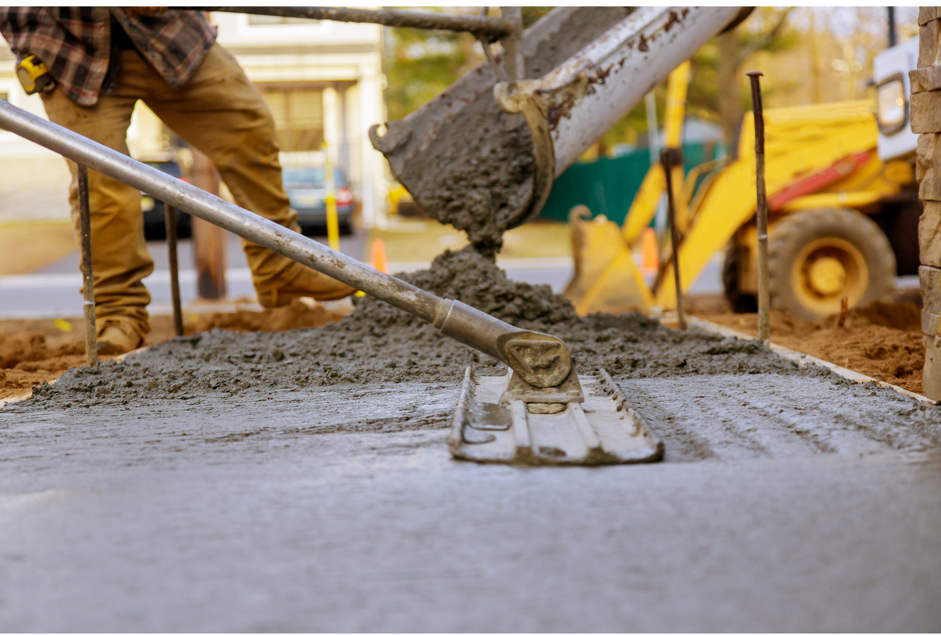A man is spreading concrete on a sidewalk with a rake.