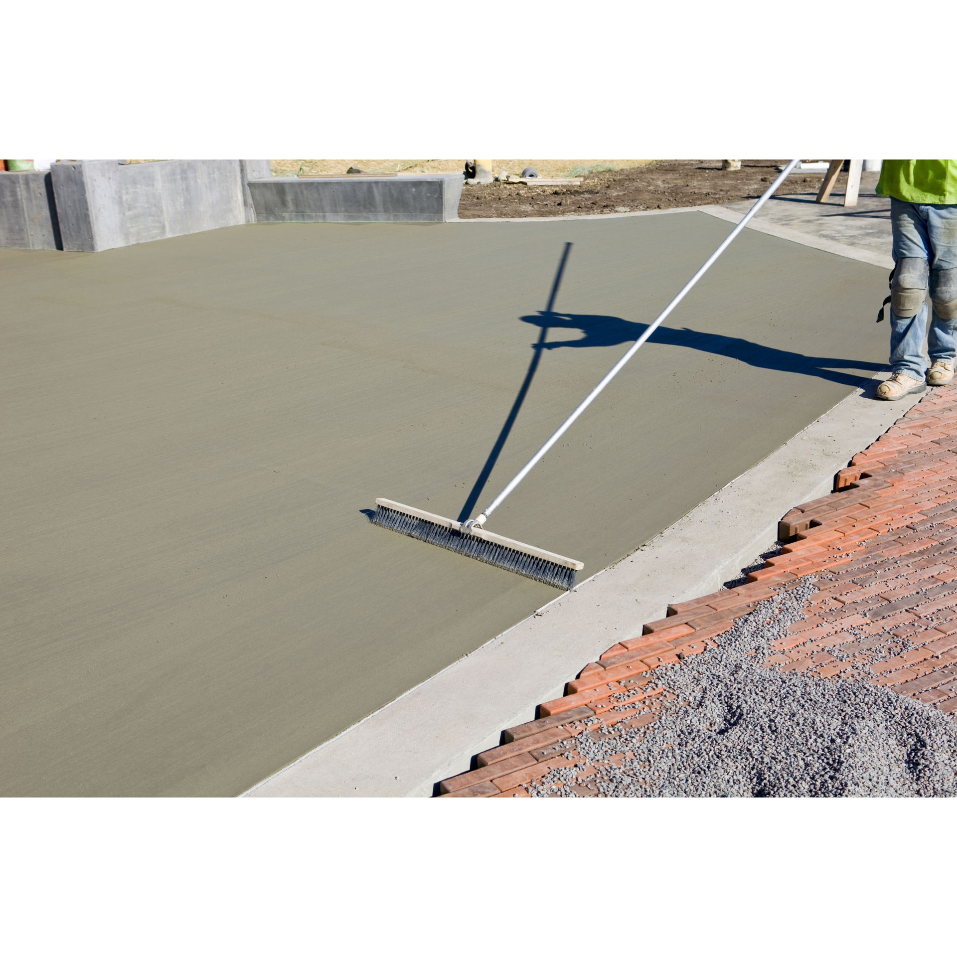 A man is using a broom to spread concrete on a construction site.
