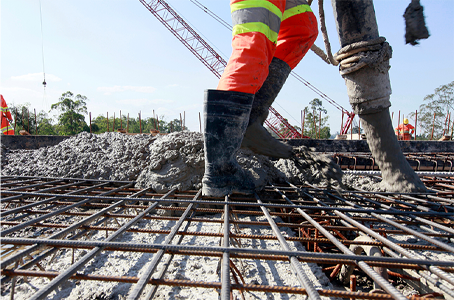 A construction worker is pouring concrete into a rebar mesh.