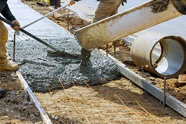 A man is pouring concrete on a sidewalk with a shovel.