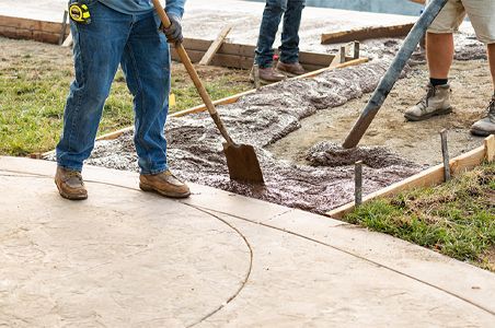 A man is using a shovel to pour concrete on a sidewalk.
