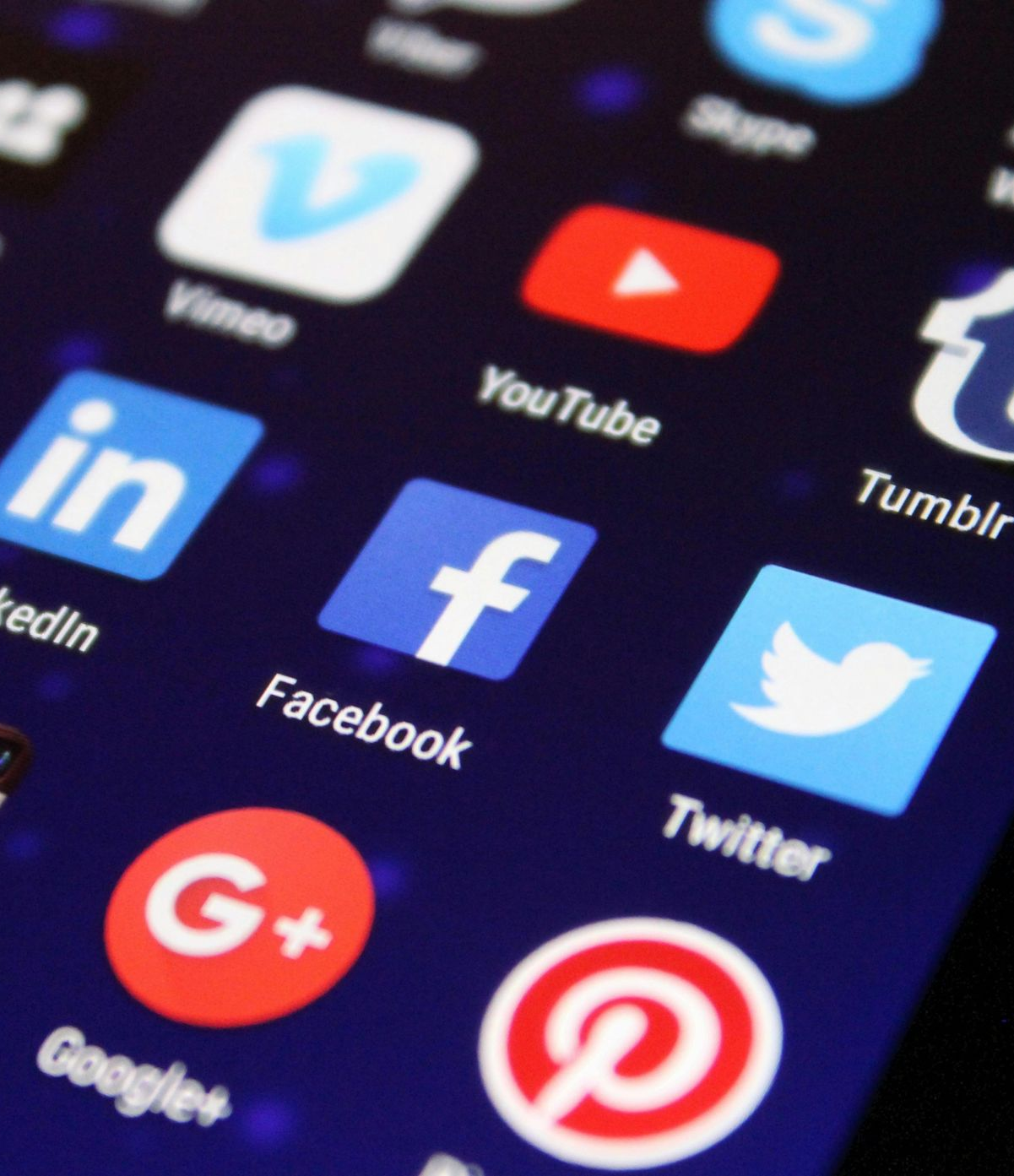 Smartphone screen displaying social media app icons: Facebook, Twitter, YouTube, and others, on a dark blue background.
