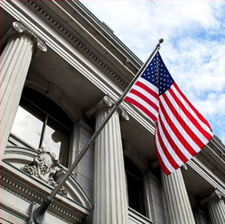 view looking up at a flag flying on the exterior of a courthouse with coloumns
