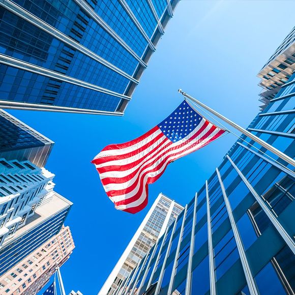 looking up at an american flag surrounded by skyscrapers