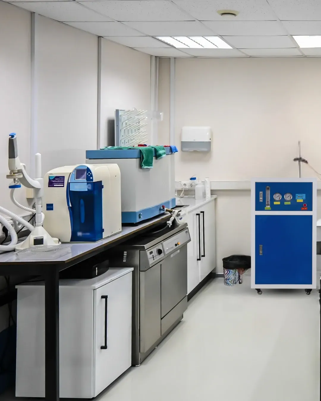 Laboratoire aux murs blancs, matériel scientifique sur un comptoir. Machines bleues et blanches, évier en acier inoxydable.