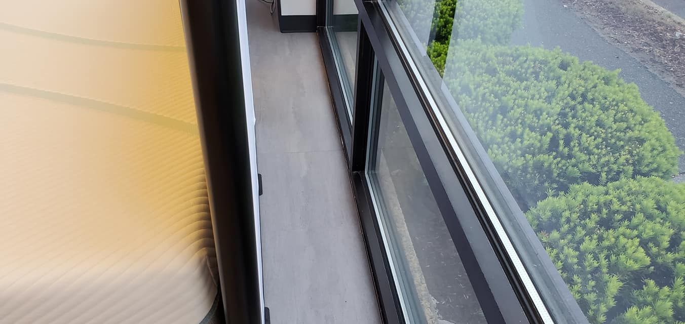 View from a balcony with glass railing overlooking green bushes and trees.