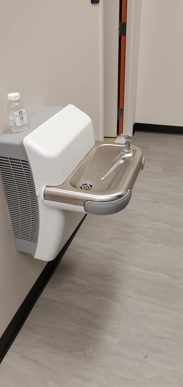 A white water fountain mounted on a wall. A plastic water bottle rests on the top.