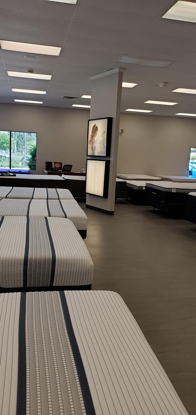 Mattress store interior with rows of mattresses on display. Display screens are mounted on a central pillar.
