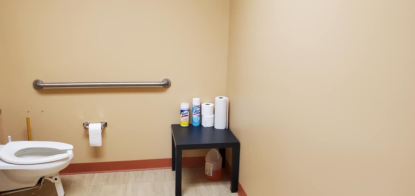 A small bathroom with a toilet, a small table with supplies, and a wall-mounted grab bar.