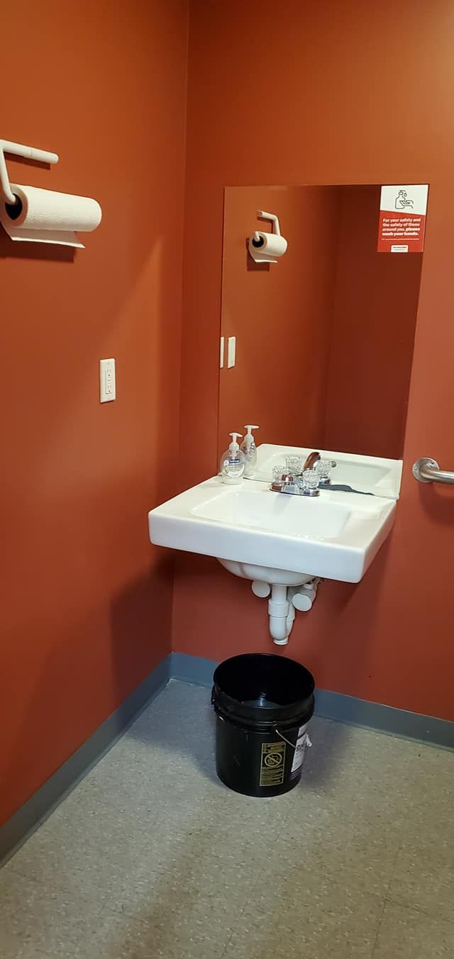 A small bathroom with a sink and mirror on red walls. A bucket sits on the floor beneath the sink.