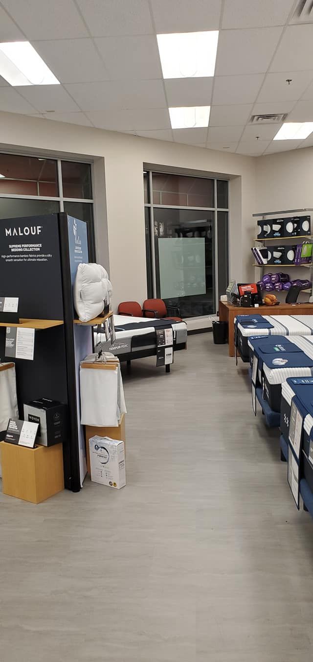 Inside a store, a long aisle with displays of products on the right.  A glass window behind a display.  Gray floor.