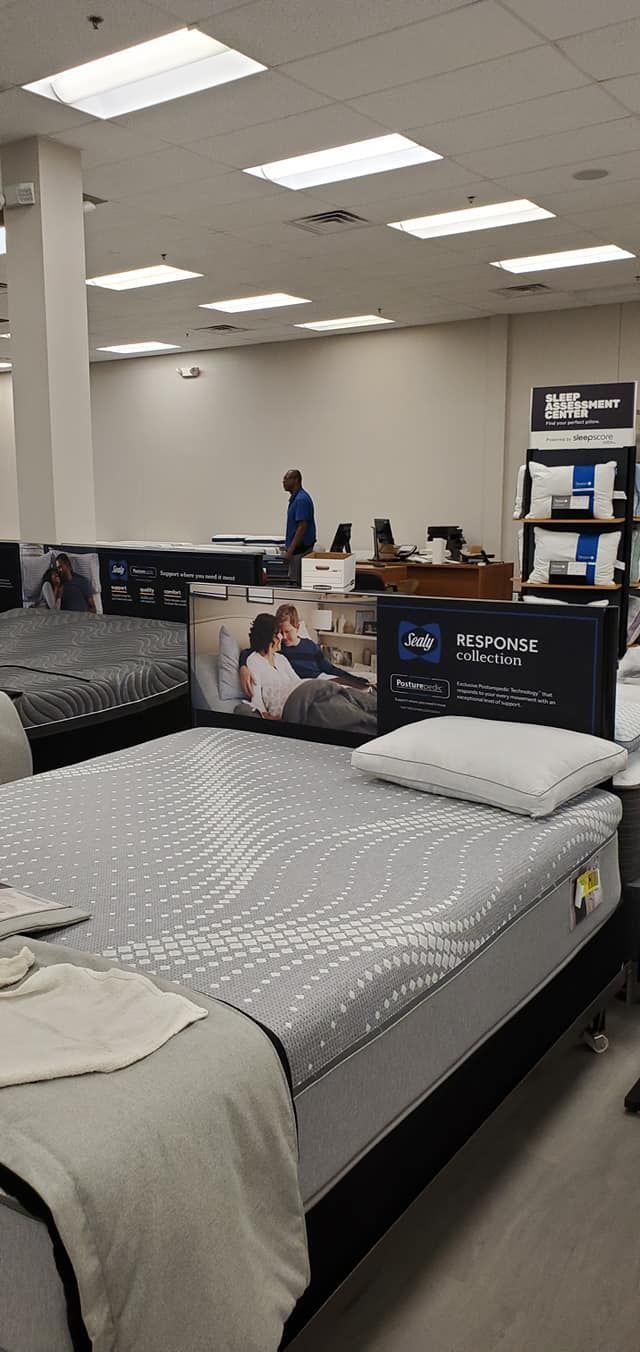 Mattresses in a showroom with customers near a desk.