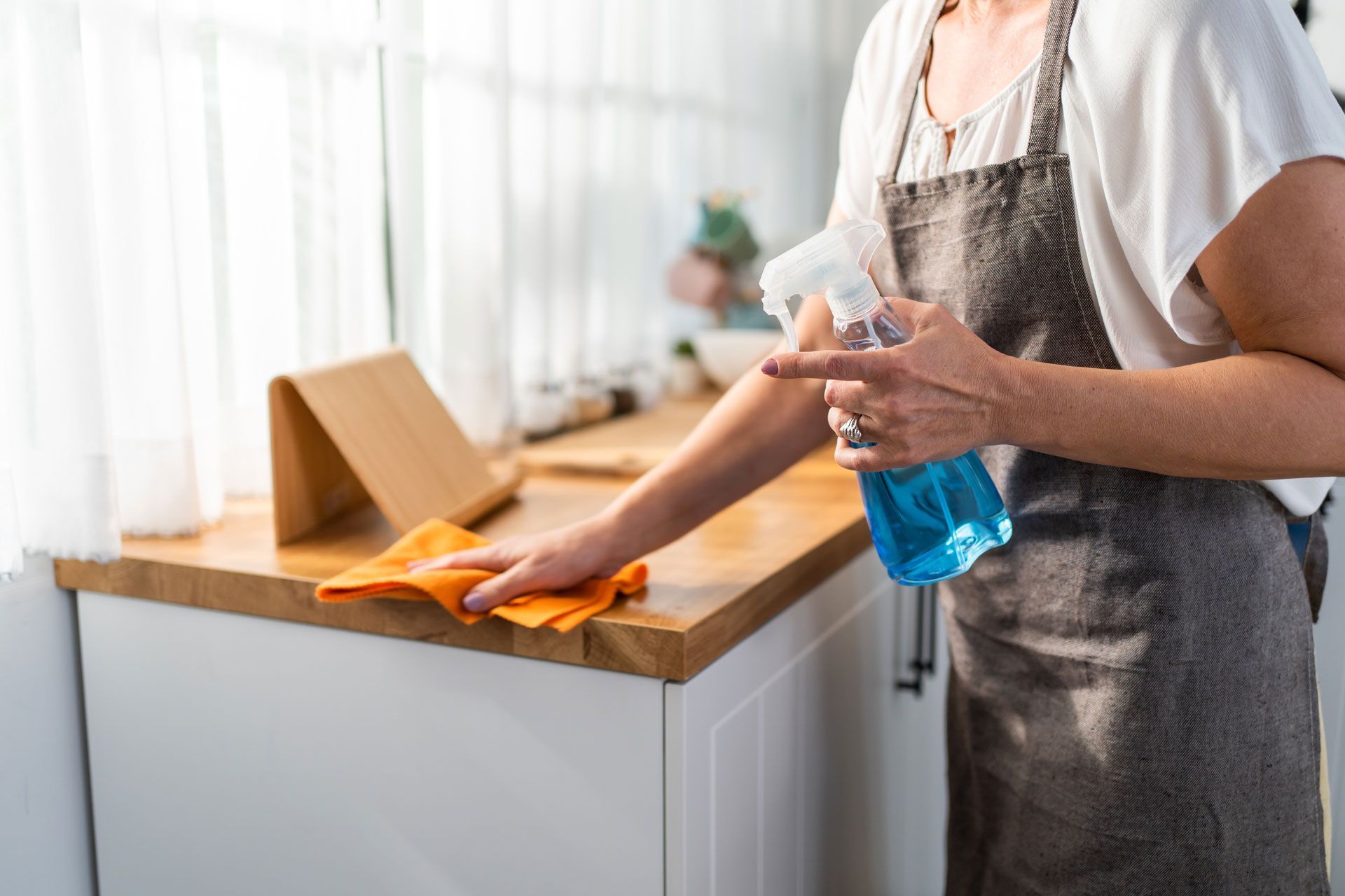 Person spraying cleaner and wiping a wooden countertop in a kitchen.