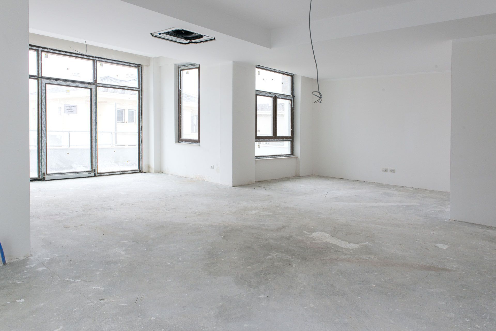 Empty, unfinished room with concrete floor, white walls, and large windows.