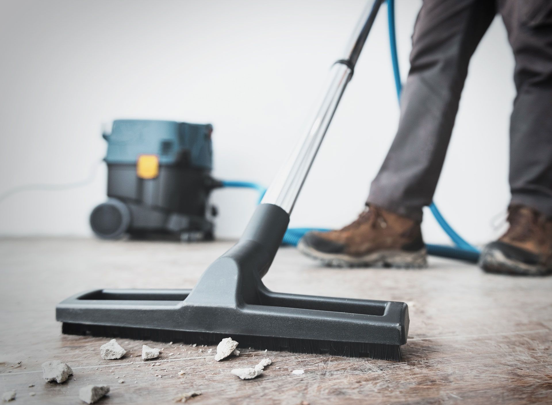 Person vacuuming a concrete floor with a shop vac, removing debris.