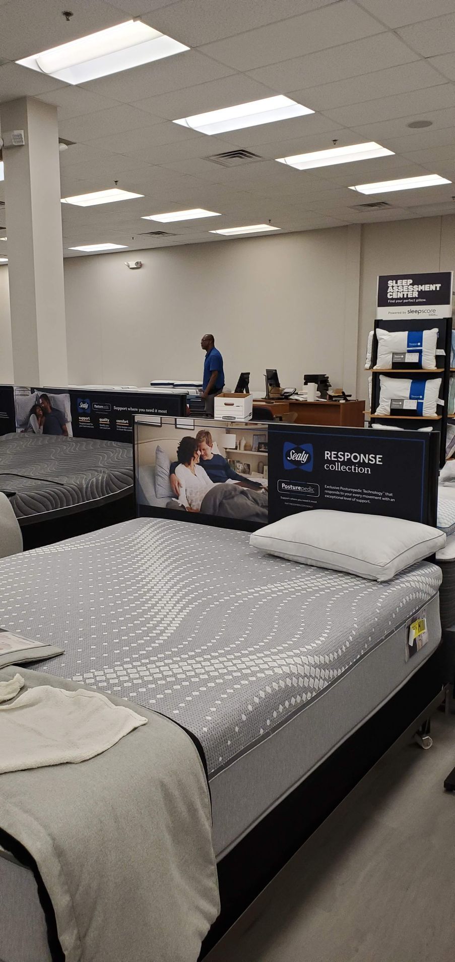 A mattress store with display beds, promotional signs, and a person in the background.