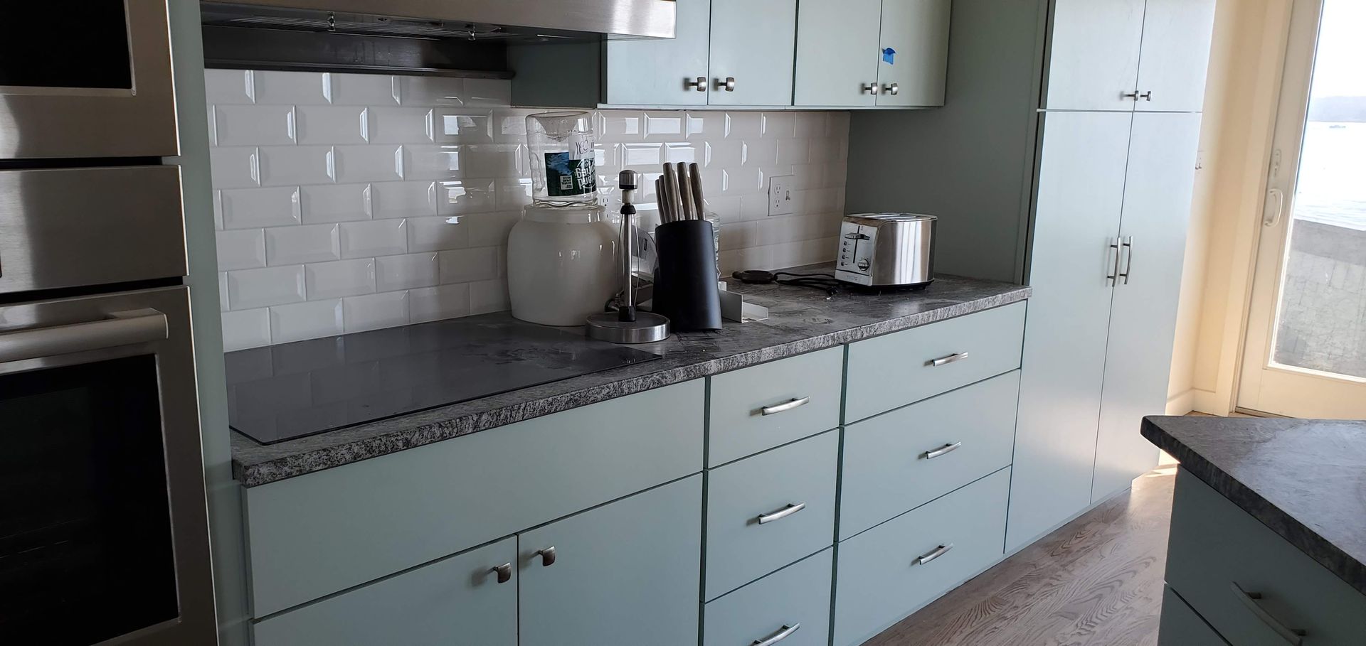 A kitchen with light blue cabinets, white subway tile backsplash, and dark granite countertops.