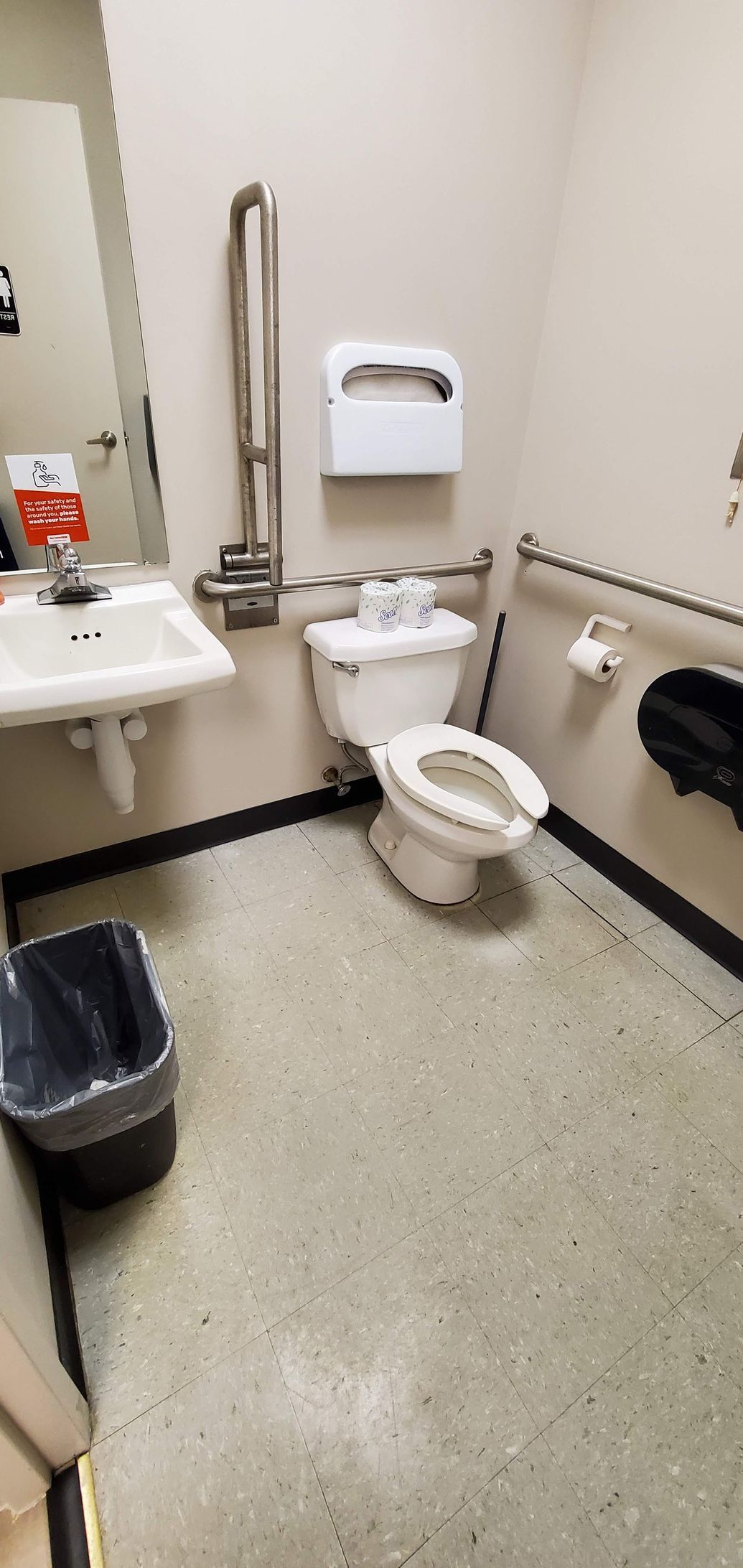 Public restroom with a toilet, sink, and trash can.