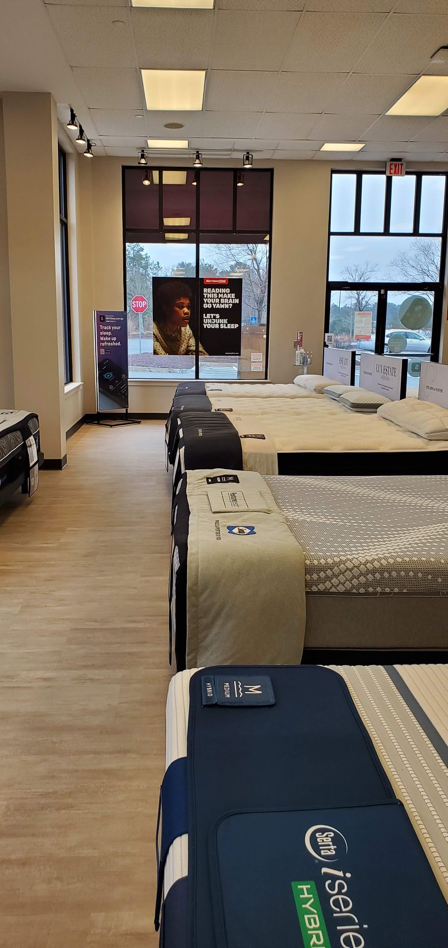 Mattress store interior with rows of beds on display near a large window.