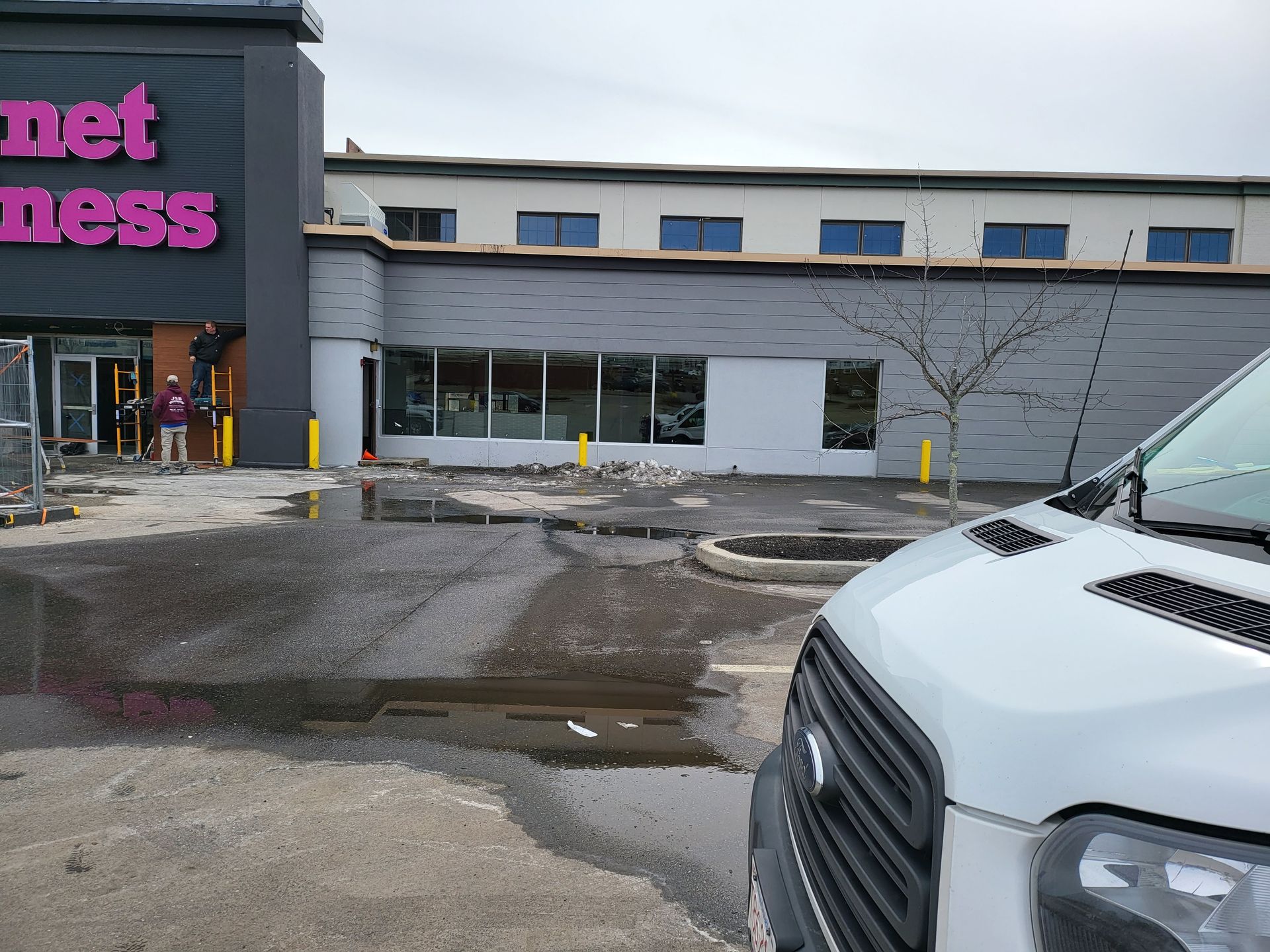 Exterior of a Planet Fitness gym with construction in progress; a white van is parked nearby.